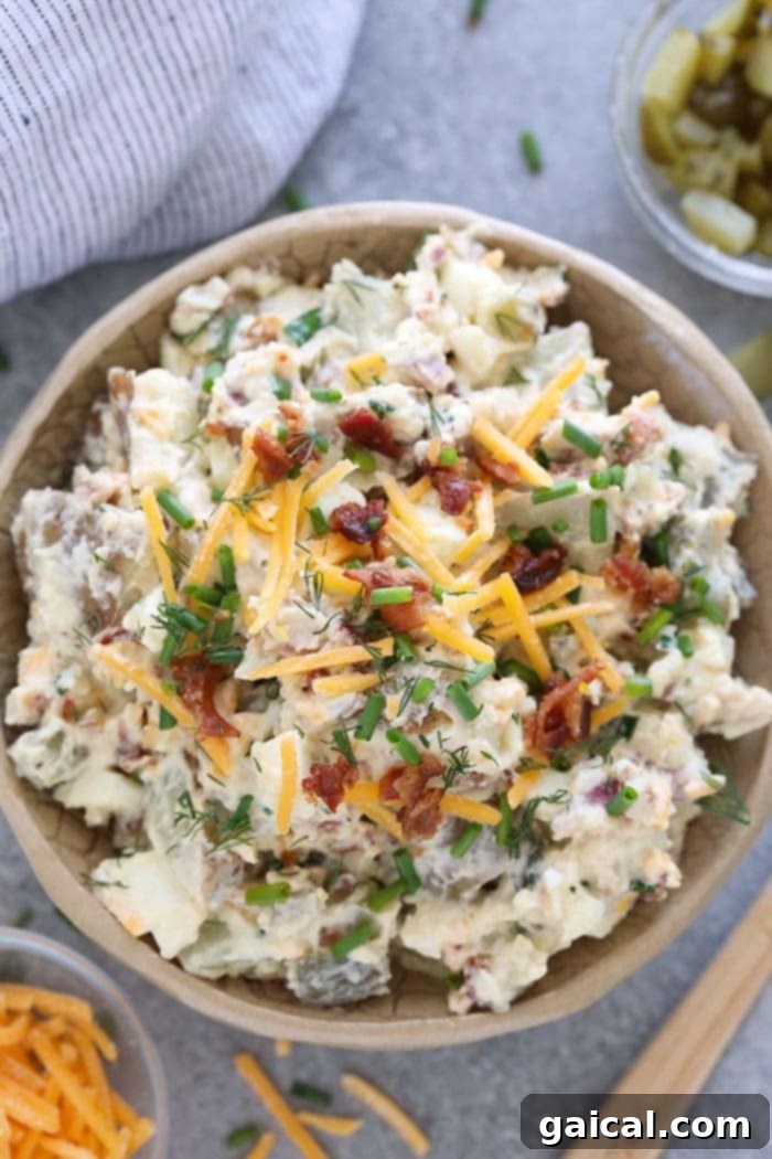 A bowl of loaded baked potato salad, garnished with fresh chives and bacon bits.
