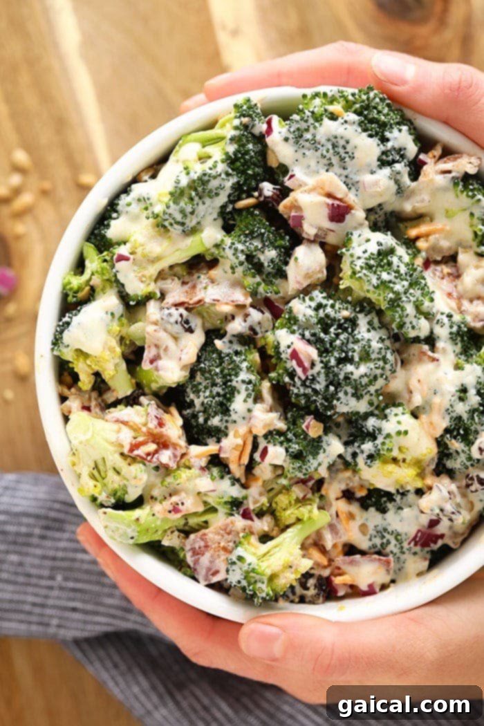 Healthy Broccoli Salad with Bacon: A Classic Midwestern Side Salad with a Healthier Twist A vibrant bowl of healthy broccoli salad with bacon, featuring fresh green broccoli florets, red onion, golden raisins, shredded cheddar cheese, and crispy bacon pieces, all coated in a creamy dressing. Perfect for a summer side dish.
