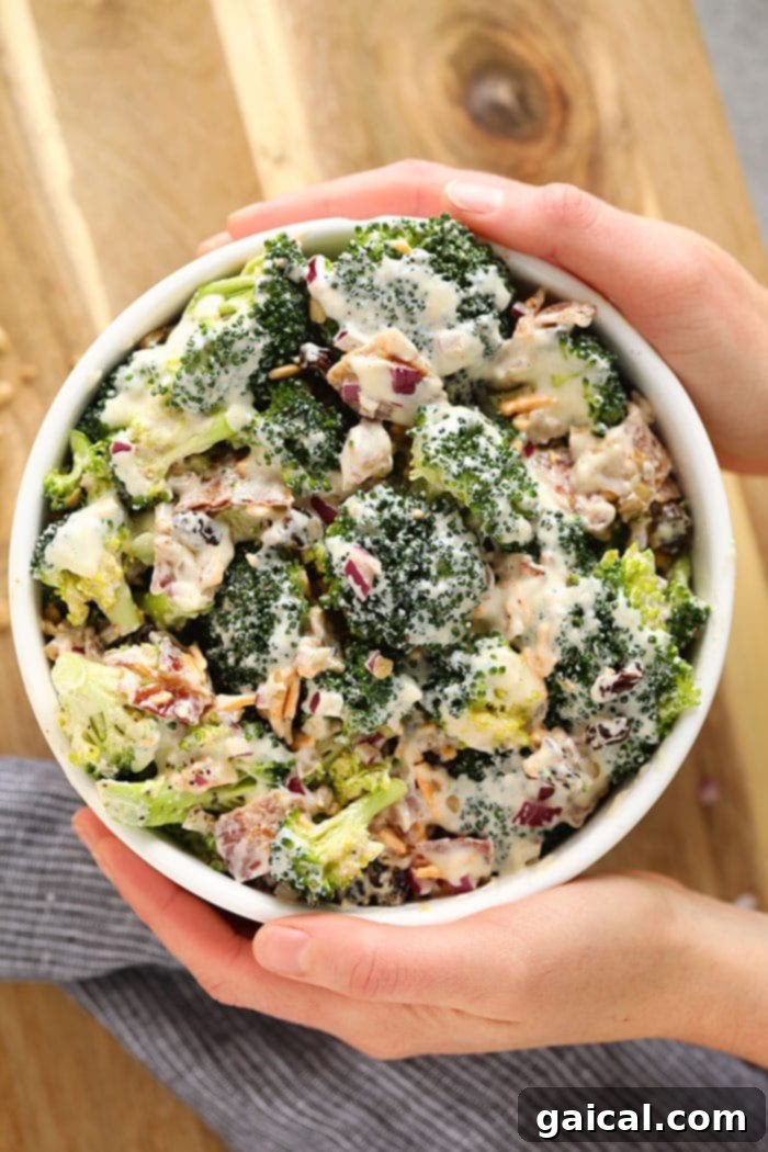 Freshly Made Healthy Broccoli Salad A beautifully presented bowl of healthy broccoli salad, showcasing a perfect blend of green broccoli florets, crispy bacon, red onion, sunflower seeds, raisins, and shredded cheddar cheese, ready to be served.