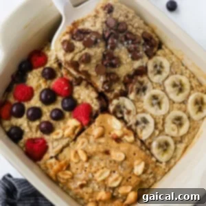 A dish of baked oatmeal is adorned with four tempting toppings: chocolate chips, banana slices, berries, and peanuts drizzled with peanut butter. A serving is being carefully lifted with a spatula, showcasing its delicious layers.