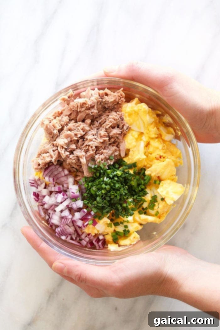 Hearty Tuna Egg Salad 4 Fresh ingredients for tuna egg salad laid out in bowls, including chopped eggs, drained tuna, red onion, chives, and creamy dressing.
