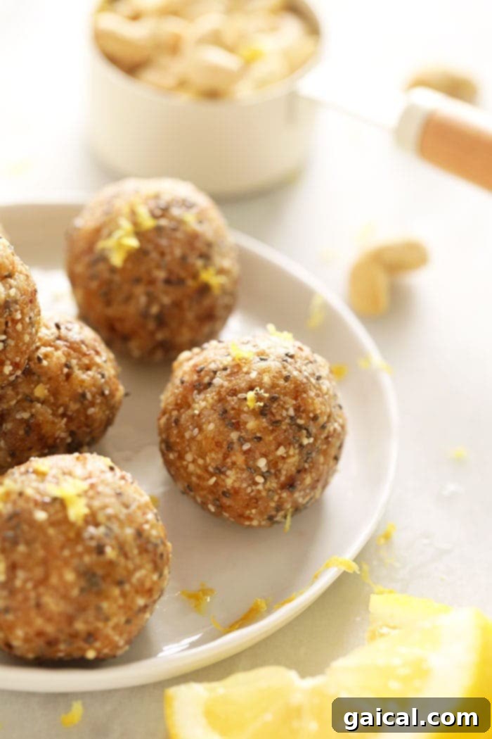 A close-up of several Lemon Cake Energy Balls on a plate, highlighted with a sprinkle of lemon zest, emphasizing their tempting appearance.