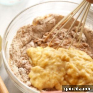 Wet ingredients being slowly added to dry ingredients in a bowl, showing the beginning of the batter mixing process.