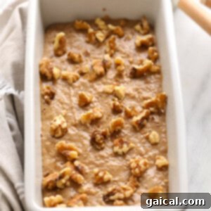 Vegan banana bread batter in a loaf pan, generously topped with chopped walnuts before baking.