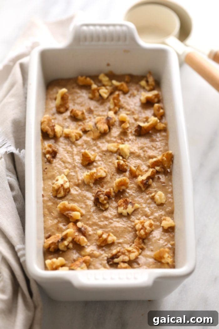 Smooth vegan banana bread batter in a loaf pan, topped with chopped walnuts, ready for baking.