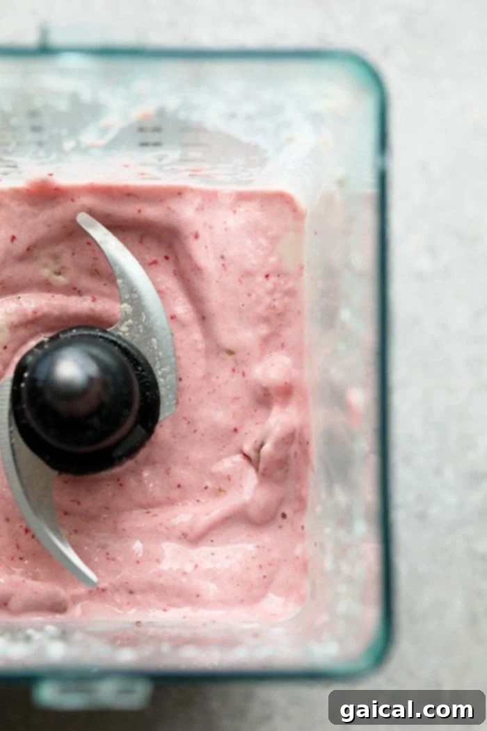 What's better than cheesecake for breakfast? NOTHING! You're going to love this Strawberry Protein Shake because it tastes exactly like strawberry cheesecake. This protein powder smoothie recipe is made with just a few simple ingredients: frozen strawberries, bananas, vanilla protein powder, Greek yogurt, and almond milk. Close-up of a creamy pink strawberry protein smoothie in a glass, with ingredients artfully arranged around it.