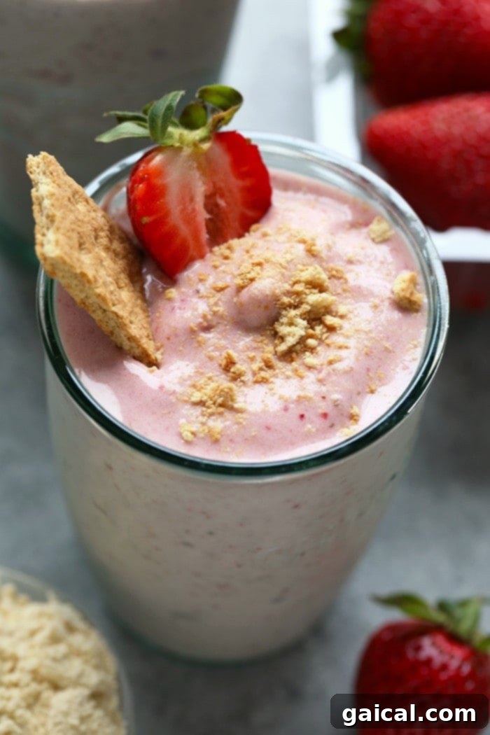 What's better than cheesecake for breakfast? NOTHING! You're going to love this Strawberry Protein Smoothie because it tastes exactly like strawberry cheesecake. This protein powder smoothie recipe is made with just a few simple ingredients: frozen strawberries, bananas, vanilla protein powder, Greek yogurt, and almond milk. A person holding a glass of strawberry protein shake, indicating freshness and enjoyment.
