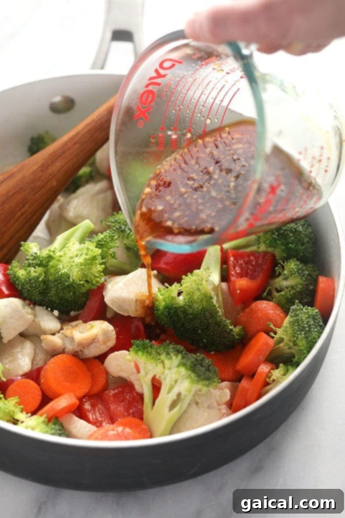 Pouring teriyaki sauce over chicken and vegetables