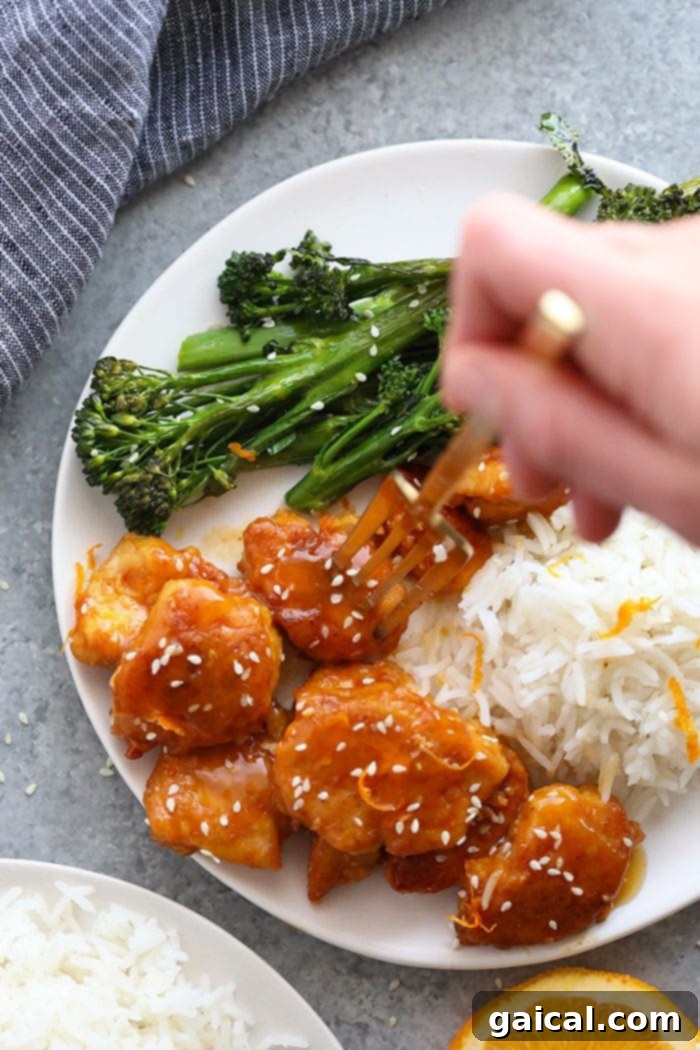 A bowl of healthy orange chicken, garnished with sesame seeds and green onions, ready to be enjoyed.