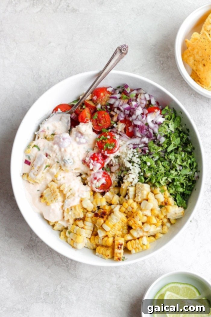 Elevate your dinner with this delicious and healthy Mexican Street Corn Salad, made with grilled corn, fresh vegetables, and a creamy cotija yogurt sauce. A large bowl of vibrant Mexican Street Corn Salad, featuring grilled corn kernels, red onion, tomatoes, fresh cilantro, and a creamy white sauce, with lime wedges on the side.