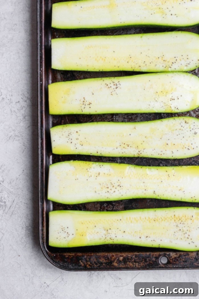 Turn on the grill and throw on some zucchini! Making grilled zucchini is easy and if you do it right you'll end up with grilled zucchini with a little crunch rather than a soggy mess. Grab the zucchini from your garden or the grocery store and get grilling! Fresh zucchini on a baking sheet, drizzled with olive oil and seasoning, ready for grilling.