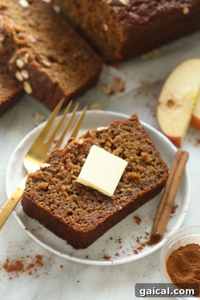 A single slice of moist cinnamon apple bread on a small plate, with a pat of butter melting on top.