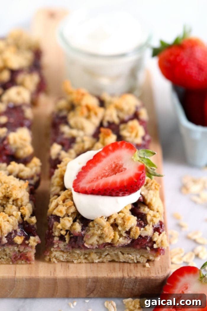 These Strawberry Oatmeal Bars are your summer dessert dreams come true! With an easy to make crust and crumble topping, and a filling made of sliced fresh strawberries reduced to perfection (with no added sugar!), these oatmeal bars are the best strawberry dessert to enjoy all summer long! Enjoy! Freshly sliced strawberry oatmeal bars arranged on a cutting board, garnished with a ripe strawberry, highlighting their irresistible layers.