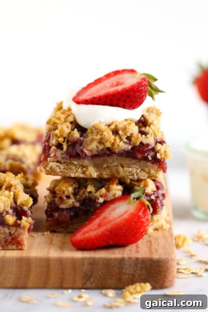 These Strawberry Oatmeal Bars are your summer dessert dreams come true! With an easy to make crust and crumble topping, and a filling made of sliced fresh strawberries reduced to perfection (with no added sugar!), these oatmeal bars are the best strawberry dessert to enjoy all summer long! Enjoy! Healthy strawberry oatmeal bars stacked neatly, adorned with fresh whole strawberries, ready to be enjoyed as a wholesome treat.