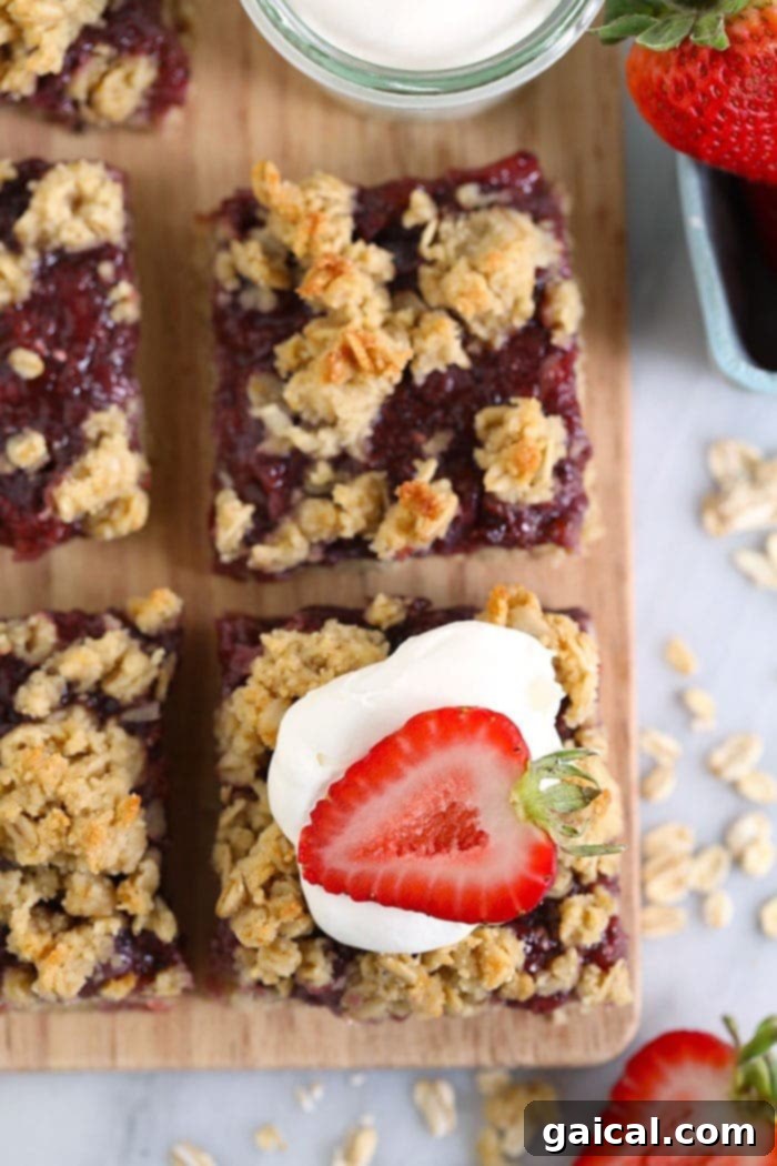 These Strawberry Oatmeal Bars are your summer dessert dreams come true! With an easy to make crust and crumble topping, and a filling made of sliced fresh strawberries reduced to perfection (with no added sugar!), these oatmeal bars are the best strawberry dessert to enjoy all summer long! Enjoy! A single sliced strawberry oatmeal bar, beautifully presented and topped with a dollop of whipped cream and a fresh strawberry slice.