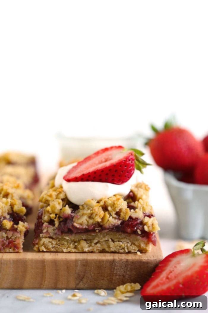 These Strawberry Oatmeal Bars are your summer dessert dreams come true! With an easy to make crust and crumble topping, and a filling made of sliced fresh strawberries reduced to perfection (with no added sugar!), these oatmeal bars are the best strawberry dessert to enjoy all summer long! Enjoy! A perfectly portioned strawberry oatmeal bar, artfully topped with fluffy whipped cream and a slice of fresh strawberry, ready to be devoured.