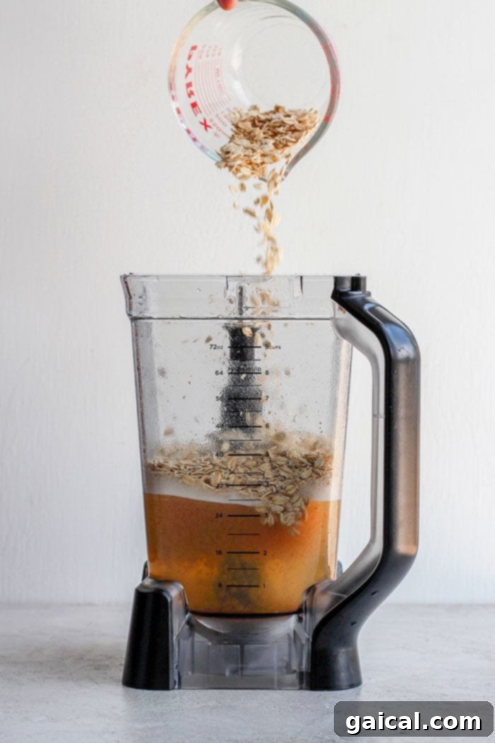 Oats for Homemade Oat Milk Close-up of old-fashioned rolled oats being carefully poured into a high-speed blender, a crucial first step in preparing creamy homemade oat milk.