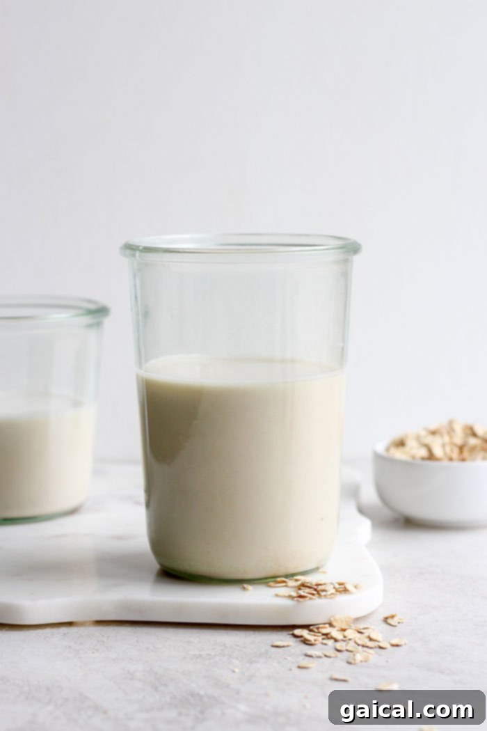 Homemade Oat Milk in a Glass A clear glass of freshly made homemade oat milk, sparkling and ready to drink, on a clean white surface.