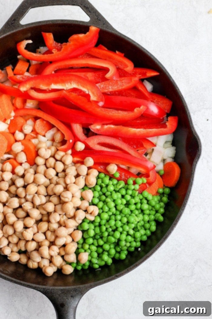 Colorful assortment of vegetables, including carrots, bell peppers, onions, and chickpeas, sautéing in a cast iron skillet.