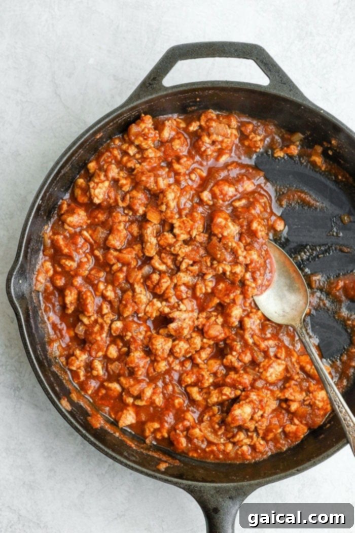 healthy sloppy joes cooking in a cast iron skillet, showing the rich sauce coating the ground chicken