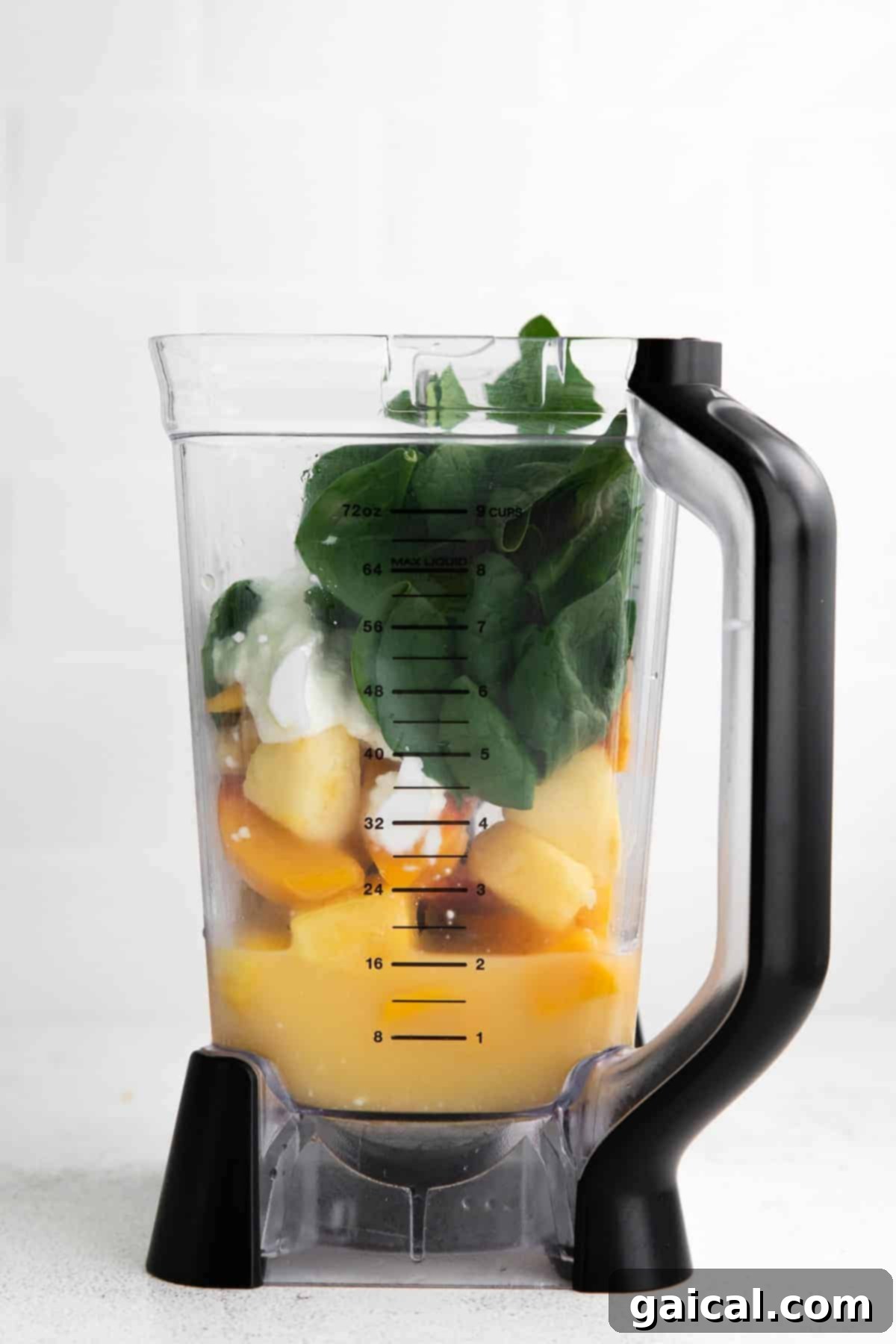 Island Green Power Smoothie 4 All the ingredients for the spinach smoothie are piled high inside a high-speed blender, ready for blending. The vibrant green spinach contrasts with the colorful frozen fruit.