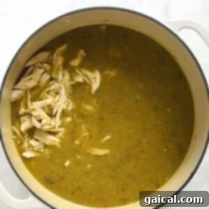 A pot of green chili soup with shredded chicken, beans, and hominy added, ready for final simmering.