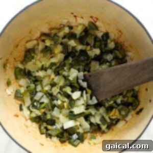 A pot filled with green chili vegetables, including onions, poblanos, and jalapeños, roasting in the oven.