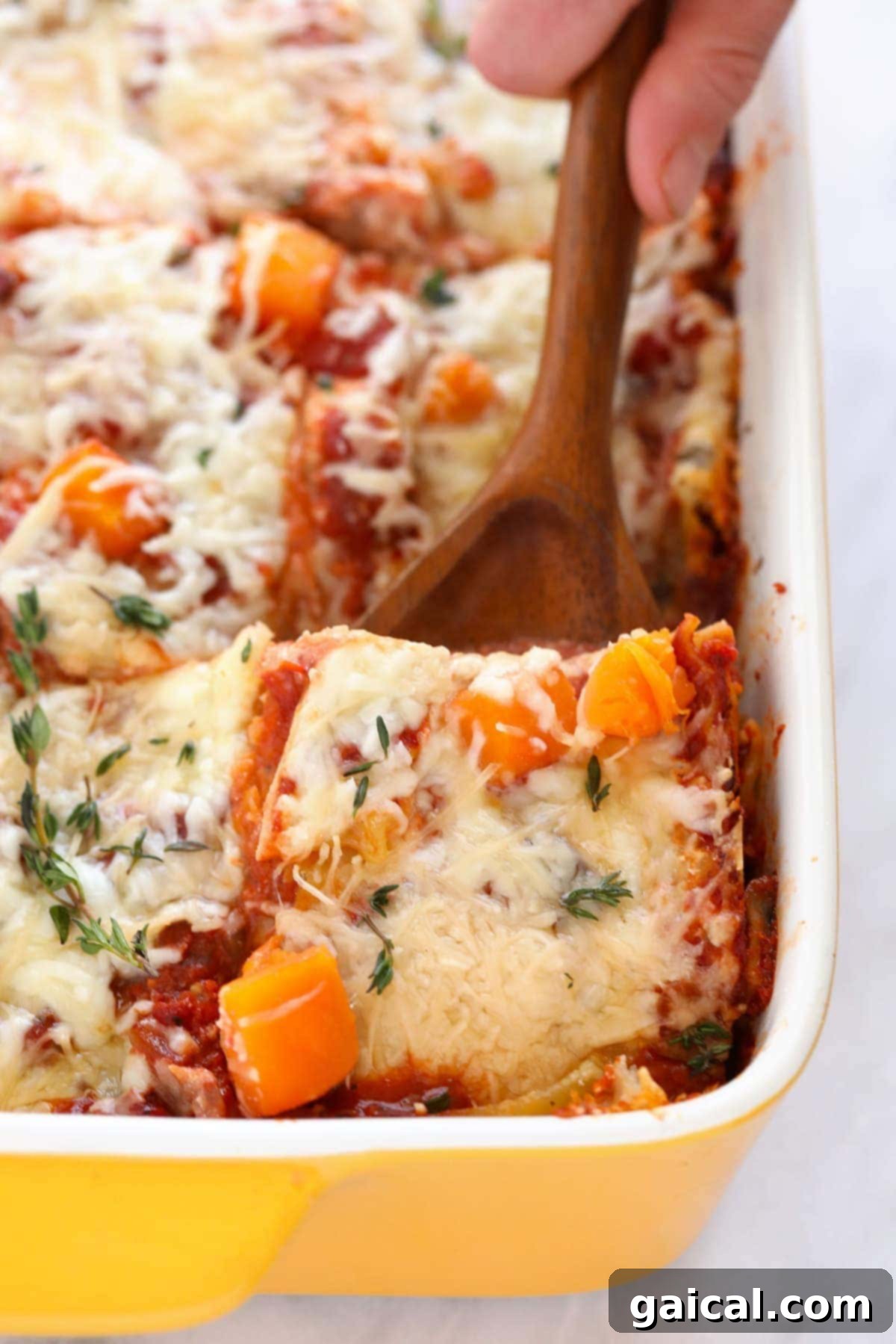 A spatula scooping out a generous piece of golden-brown butternut squash lasagna, revealing its vibrant layers.