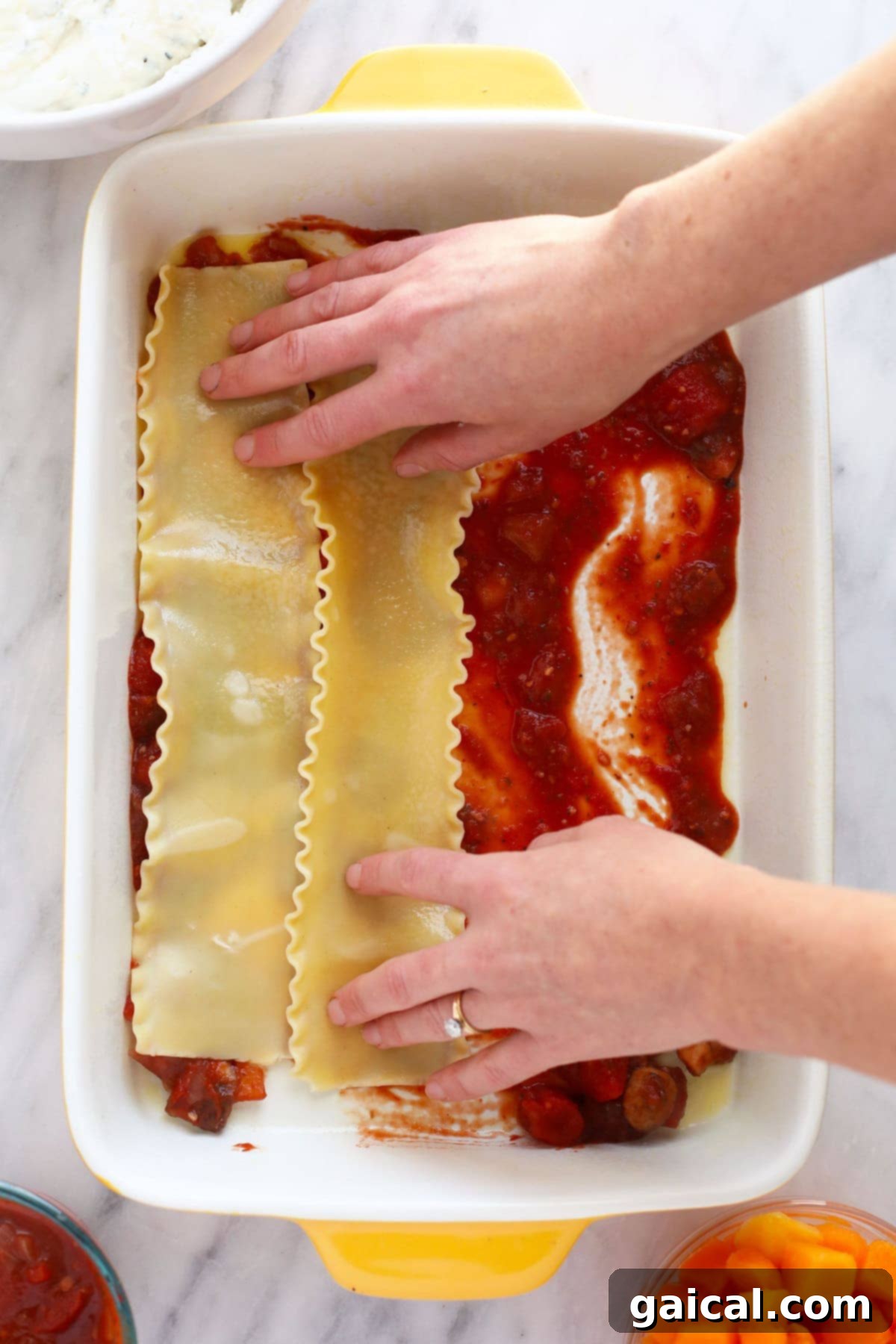Hands carefully placing a layer of lasagna noodles into a 9x13-inch casserole dish, preparing for the next delicious layer.