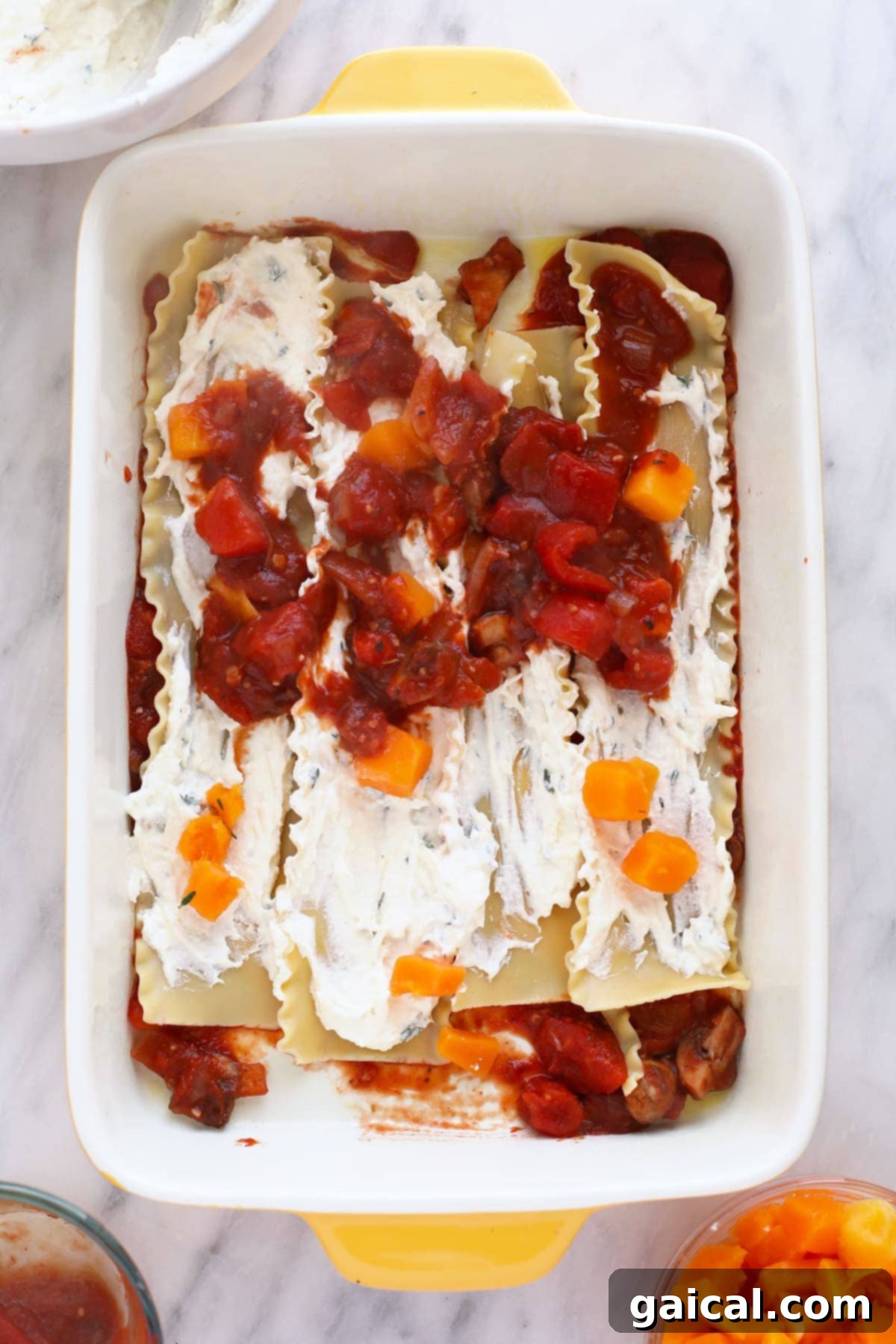 A partially assembled butternut squash lasagna in a 9x13 pan, showing the layers of noodles, sauce, and cheese.