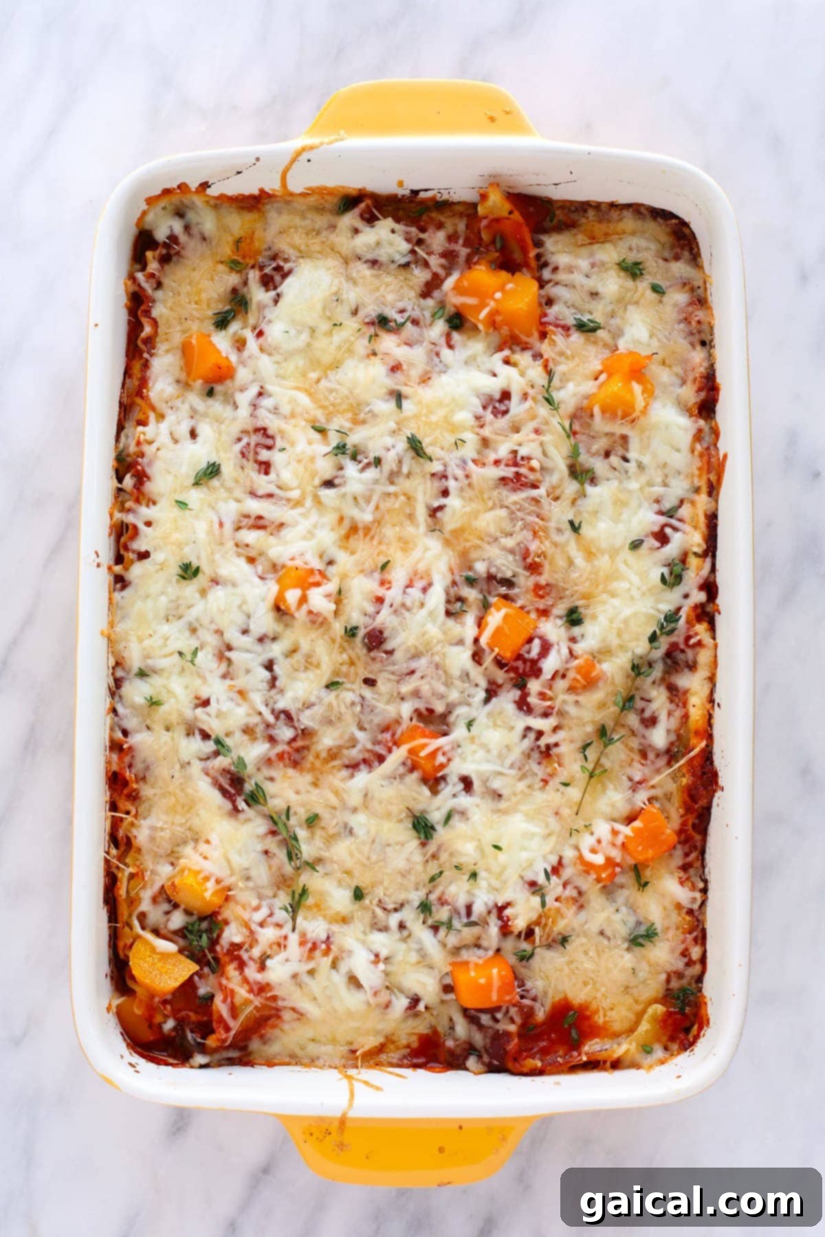 A baked butternut squash lasagna, golden brown on top, garnished with fresh thyme, ready to be served.