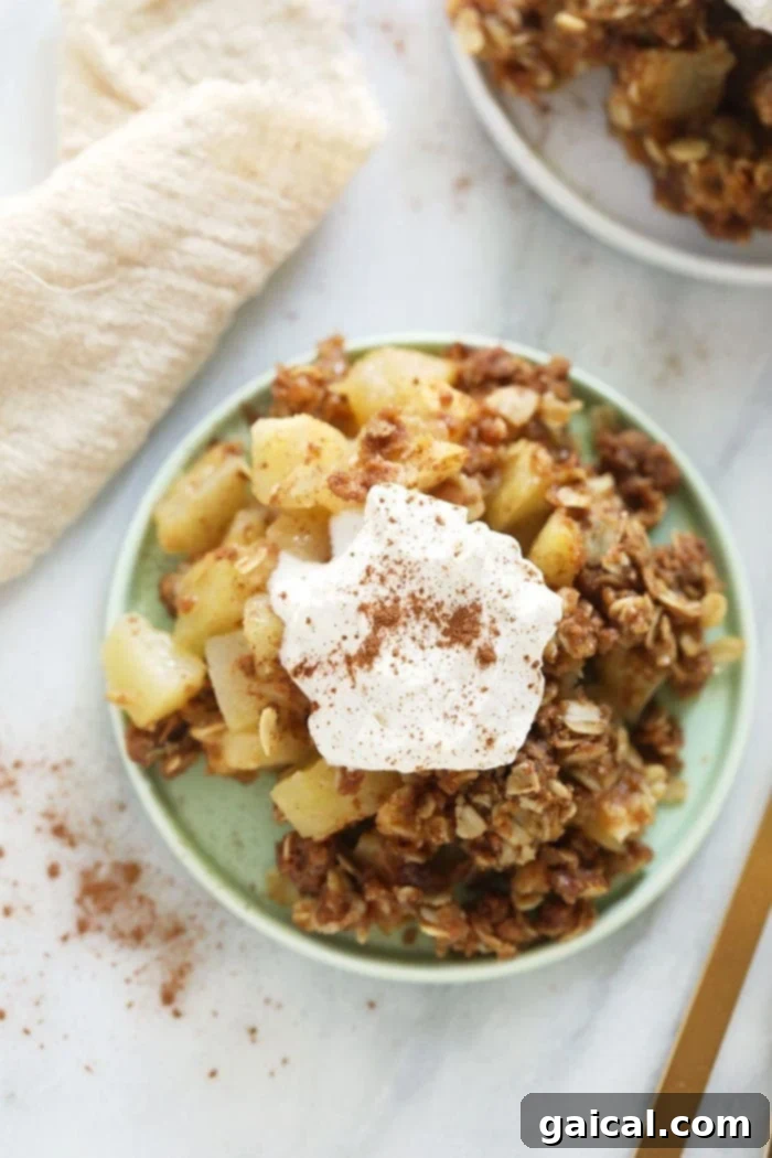 This delicious apple crisp recipe is made with a simple apple filling and a delicious crumble topping. Make this healthier, fall-inspired dessert today! A serving of warm apple crisp on a white plate, topped with a generous scoop of melting vanilla ice cream, showing the contrast between the golden-brown topping and the soft apple filling.