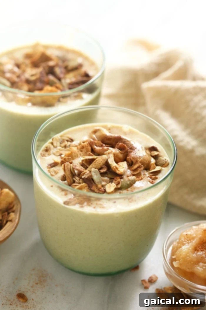 This apple smoothie recipe is an excellent healthy breakfast idea or snack. It's made with frozen applesauce, almond milk, ground flaxseed, and your favorite nut butter. A vibrant apple smoothie in a glass, garnished with crunchy granola and a sprinkle of cinnamon, ready to be enjoyed.