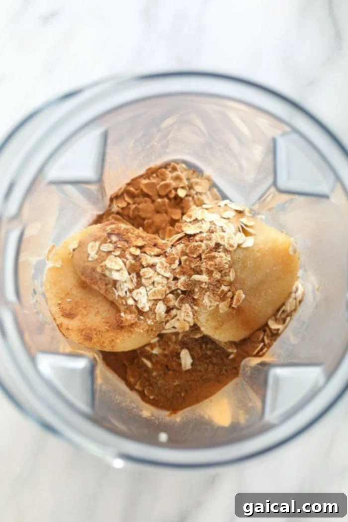 Crisp Apple Blend 2 All the fresh ingredients for the apple smoothie, including frozen applesauce cubes, almond milk, oats, and cinnamon, arranged perfectly in a blender before blending.