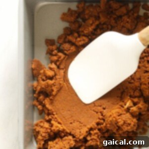 A white spatula being used to press the gingersnap crust into a baking pan.