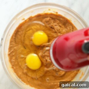Adding two eggs to a bowl of pumpkin cheesecake filling mixture.