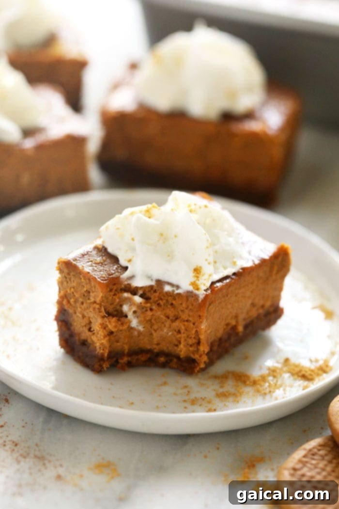 A close-up of a pumpkin cheesecake bar with a bite taken out, revealing the perfectly layered gingersnap crust and smooth, spiced pumpkin filling.