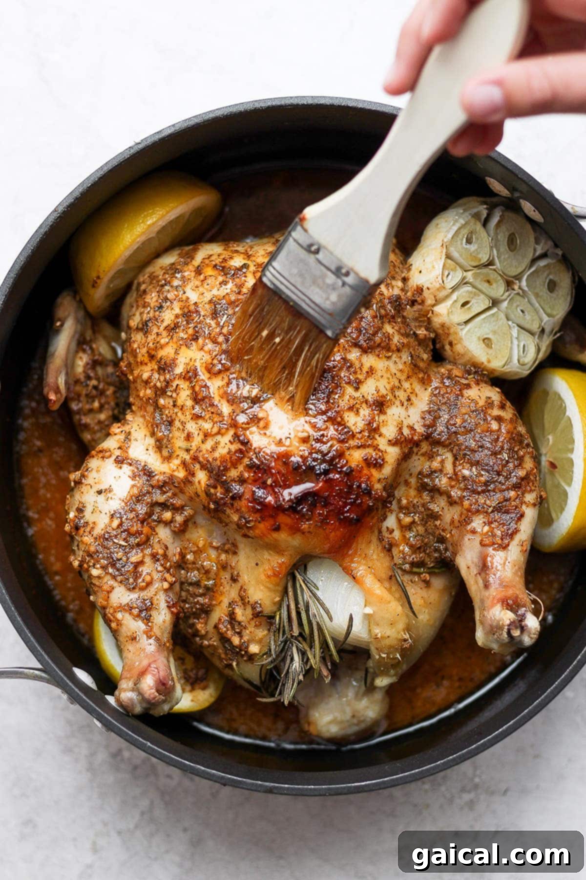 A chef uses a basting brush to generously coat a roasted whole chicken with pan juices, ensuring moisture and flavor.