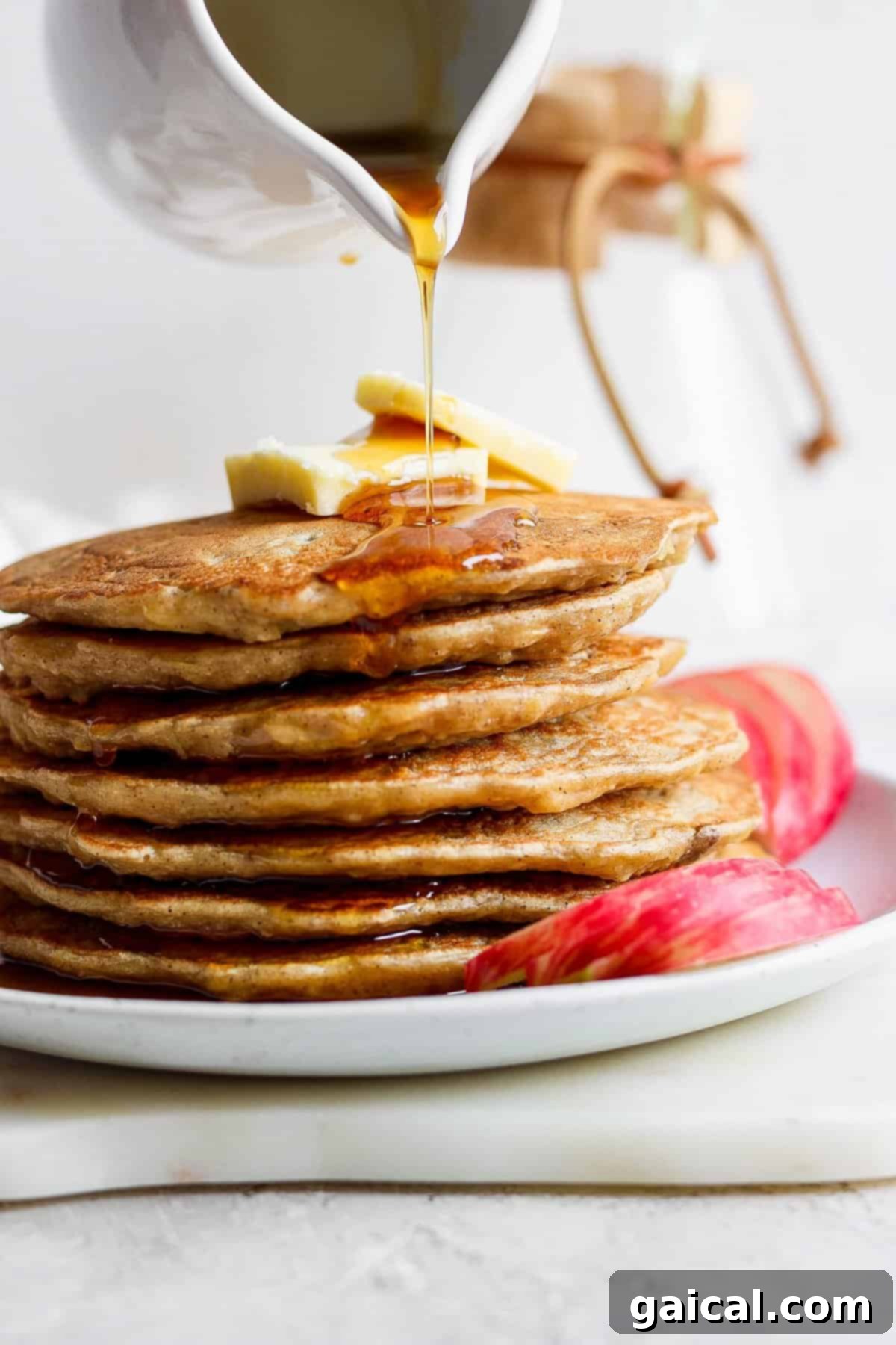 A stack of golden brown apple pancakes with warm syrup being poured over them.