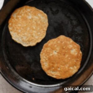 Two apple pancakes cooking in a cast iron skillet on a stovetop.