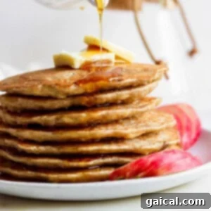 A stack of warm apple pancakes with syrup being drizzled over them.