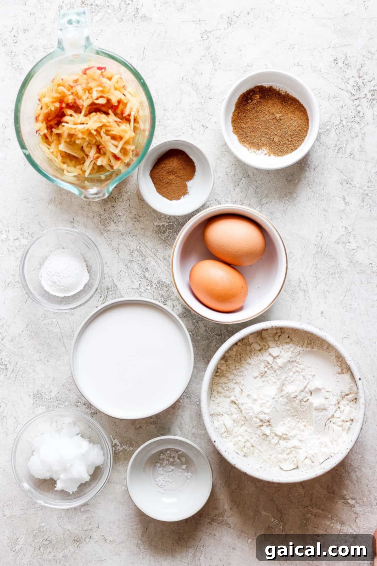 Fresh ingredients for apple pancakes laid out on a wooden table, including eggs, flour, sugar, and apples.