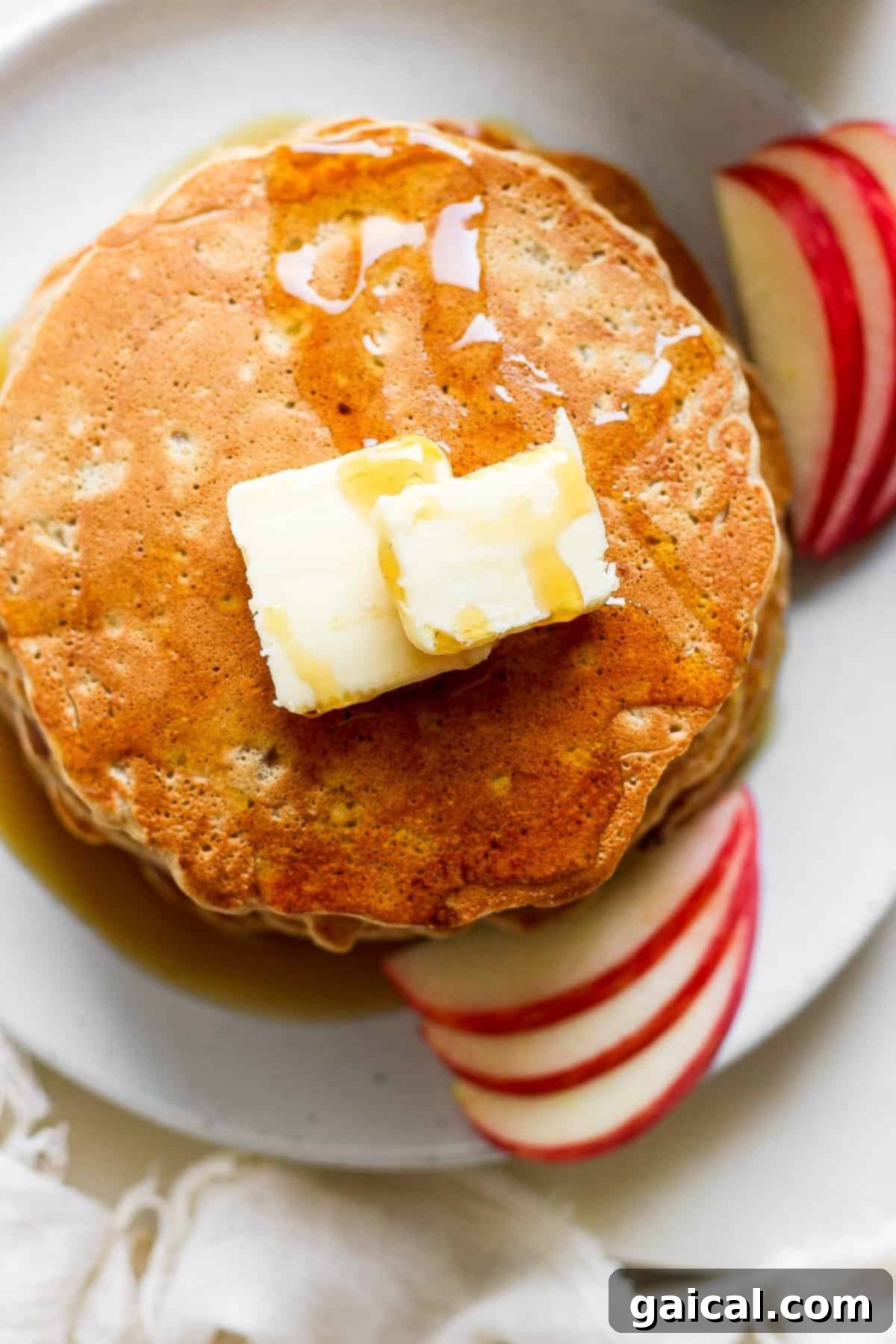 A plate of fluffy pancakes topped with butter and fresh apple slices.