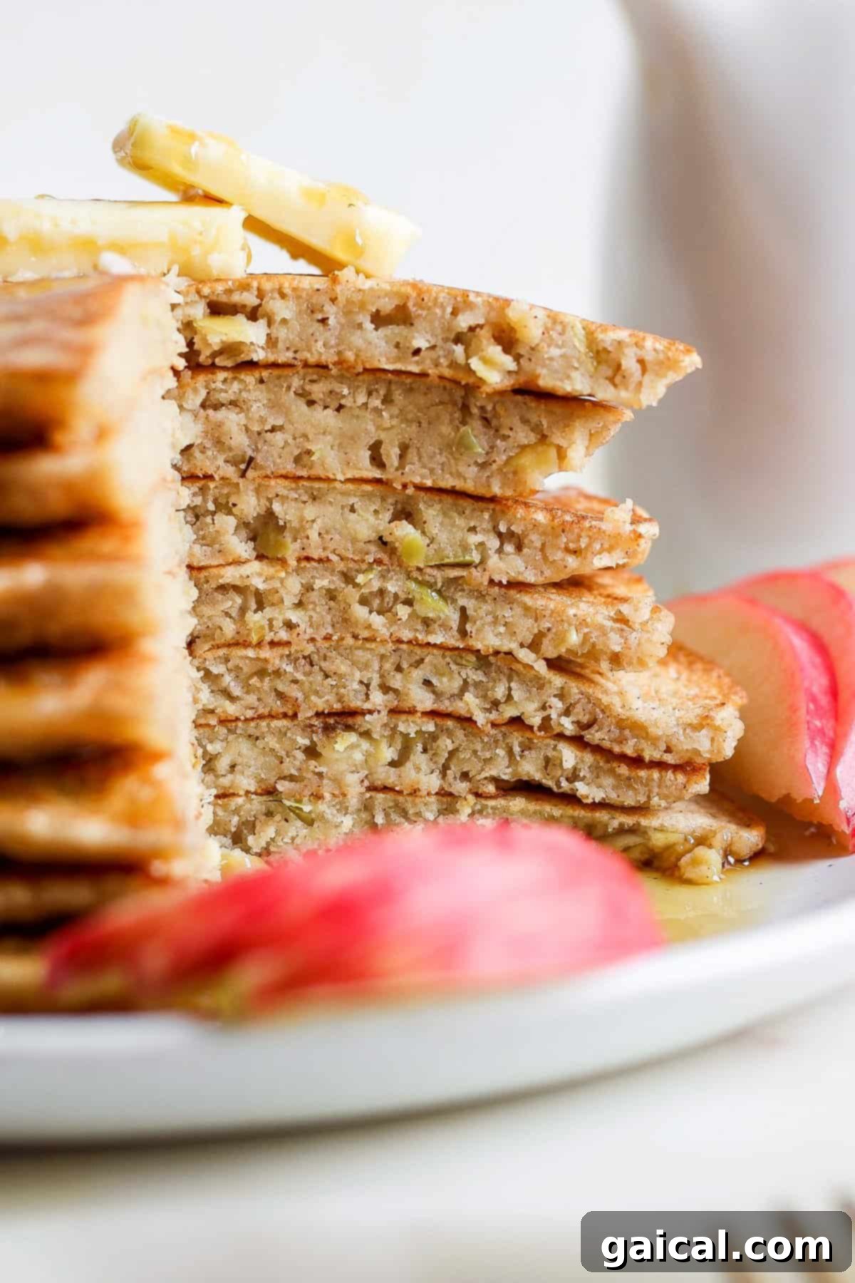 A beautifully arranged plate of stacked pancakes with apple slices and a drizzle of syrup.