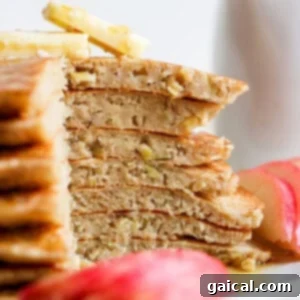 A stack of pancakes on a plate with apple slices.