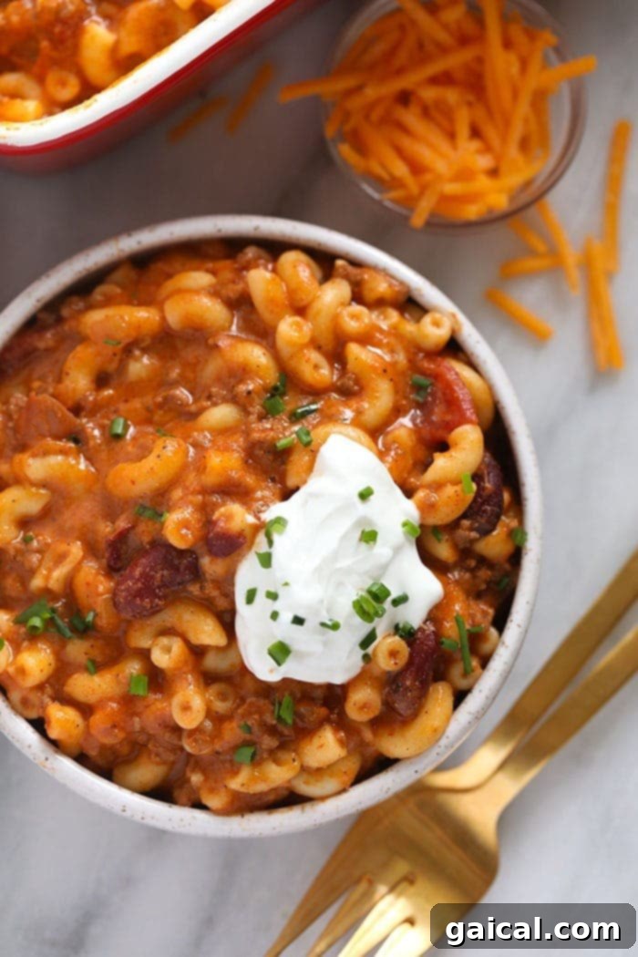 Delicious Chili Mac served with cooling Greek yogurt and fresh herbs. A bowl of hot Chili Mac and Cheese topped with a dollop of creamy Greek yogurt and fresh green onions.