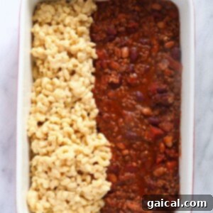 A casserole dish with chili and macaroni and cheese mixed together, ready for baking.