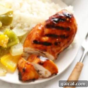 A plate with perfectly grilled teriyaki chicken alongside rice and fresh vegetables.