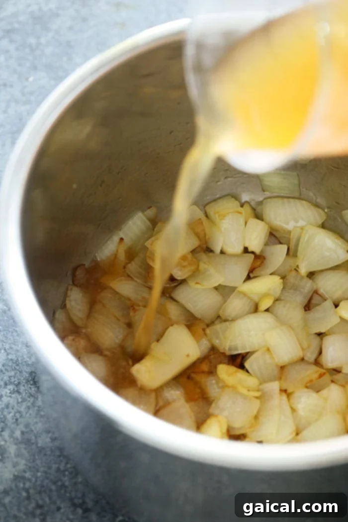 Building Flavor: Sautéing Aromatics for Your Butternut Squash Soup Base Fragrant sautéed onions and garlic, glistening in olive oil, with vegetable broth being poured into the Instant Pot, forming the savory base for the butternut squash soup.