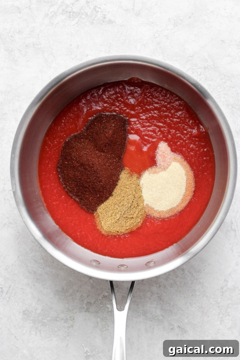 Homemade Enchilada Sauce simmering in a saucepan on the stove, showing its rich, glossy texture.